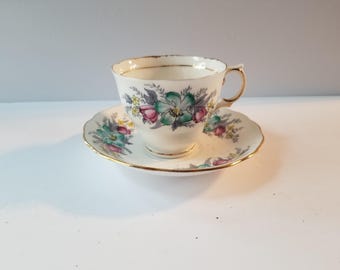May include: A vintage teacup and saucer set with a floral pattern in shades of pink, green, and yellow. The cup and saucer have a gold trim.