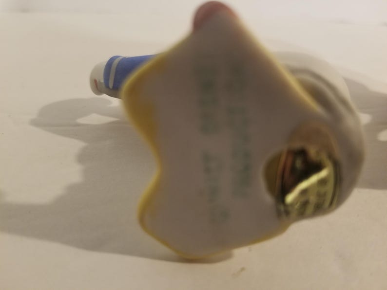 Puede incluir: Una figurita de porcelana de una ni&ntilde;a con un traje de marinero azul y blanco. La figurita est&aacute; de pie sobre una base blanca con una pegatina dorada que dice "The Bradford Exchange, 1992".