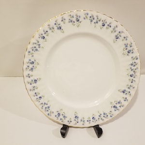 Peut inclure: Une assiette plate en céramique blanche avec un motif floral bleu et vert autour du bord. L'assiette a une bordure dorée.