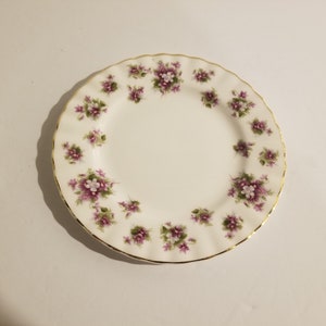 May include: A white ceramic plate with a gold rim and a floral pattern of purple and white flowers.
