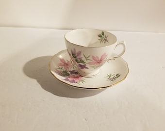 May include: A white teacup and saucer with a floral pattern in shades of pink and purple. The cup and saucer have a gold trim.