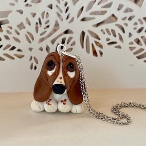 Puede incluir: Un collar con un dije de perro basset marrón y blanco. El perro está hecho de arcilla polimérica y tiene una cadena de plata.