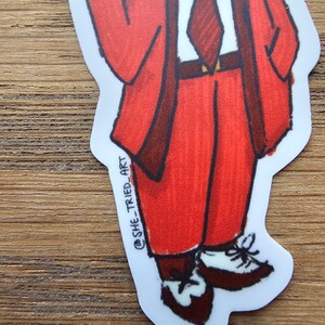 May include: A cartoon illustration of a person wearing a red suit, a white shirt, and a dark red tie. The person is wearing brown shoes with white laces. The illustration is on a white background with the text "@SHE_TRIED_ART" in the lower left corner.