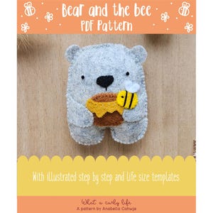 Op de afbeelding: Een grijze vilten beer die een honingpot en een bij vasthoudt. De beer heeft een zwarte neus en ogen. De honingpot is bruin en geel, en de bij is geel en zwart. De afbeelding bevat de tekst "Bear and the bee PDF Pattern".