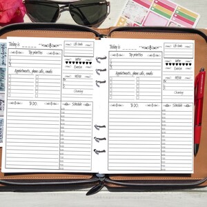 Puede incluir: Agenda abierto con p&aacute;ginas en blanco para la programaci&oacute;n diaria. Las p&aacute;ginas est&aacute;n dentro de un estuche de cuero marr&oacute;n. Tambi&eacute;n son visibles pegatinas, un bol&iacute;grafo rojo y gafas de sol. El planificador incluye secciones para citas, listas de tareas y horarios.