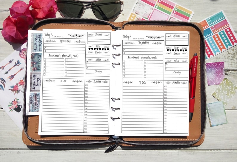 Puede incluir: Agenda abierto con p&aacute;ginas en blanco para la programaci&oacute;n diaria. Las p&aacute;ginas est&aacute;n dentro de un estuche de cuero marr&oacute;n. Tambi&eacute;n son visibles pegatinas, un bol&iacute;grafo rojo y gafas de sol. El planificador incluye secciones para citas, listas de tareas y horarios.