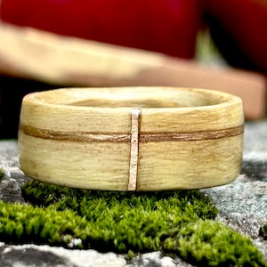 May include: A wooden ring with a light brown finish and thin gold lines. The ring has a vertical gold line in the center.
