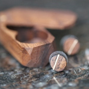 May include: A wooden box with a hinged lid, open to reveal two small wooden rings with a thin gold line around the edge.