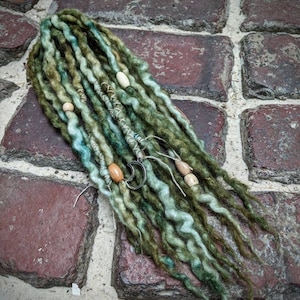 Op de afbeelding: Groene en blauwe synthetische dreadlocks met houten kralen en metalen ringen.
