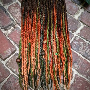 May include: A set of long, colorful dreadlocks with brown, green, orange, and red tones. The dreadlocks are decorated with wooden beads.