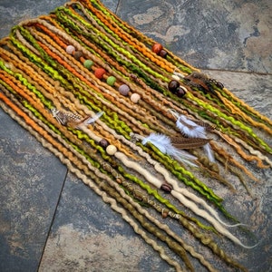 May include: A set of colourful synthetic dreadlocks with beads and feathers. The dreadlocks are in shades of green, brown, orange, and beige.