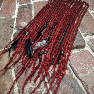 May include: Red, brown, and black synthetic dreadlocks with red and brown beads. The dreadlocks are arranged in a long, flowing style.