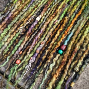 May include: A set of long, colourful synthetic dreadlocks with beads and charms. The dreadlocks are made of wool and are in shades of green, brown, and purple.