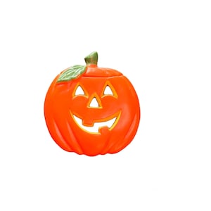 May include: A ceramic orange pumpkin with a smiling face, triangular eyes, and a green stem and leaf. The pumpkin is a Halloween decoration, likely used as a candy holder or decorative piece.