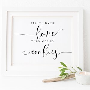 Peut inclure: Impression encadrée blanche avec un texte en calligraphie noire qui dit "D'abord vient l'amour, puis viennent les biscuits".