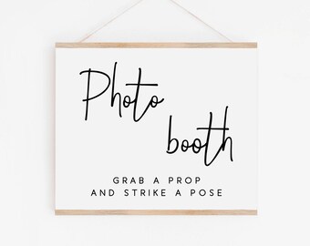 May include: A white sign with black text that reads "Photo booth" and "Grab a prop and strike a pose". The sign is hanging from a wooden frame.