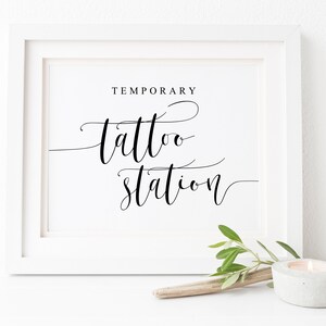 Puede incluir: Un cartel blanco enmarcado con texto en caligraf&iacute;a negra que dice "Temporary Tattoo Station".