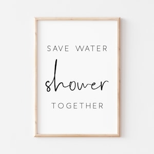 Op de afbeelding: Een witte ingelijste print met zwarte tekst die "Save Water Shower Together" luidt.