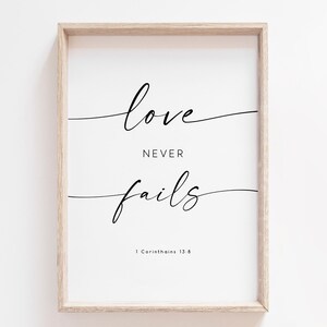 Op de afbeelding: Een ingelijst print met de tekst "liefde gaat nooit voorbij" in een eenvoudig, elegant lettertype. De tekst is gecentreerd op een witte achtergrond en wordt vergezeld door een bijbelverwijzing: "1 Korintiërs 13:8".