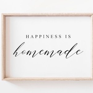 Pode incluir: Uma impressão emoldurada com o texto "Happiness is homemade" em uma fonte preta simples em um fundo branco.