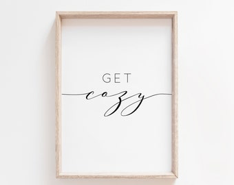 May include: A framed print with the text "GET cozy" in a simple, modern font. The print is in a light wood frame and has a white background.