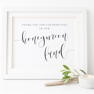 Pode incluir: Um sinal branco emoldurado com texto preto que diz "Obrigado por contribuir para o nosso fundo de lua de mel".