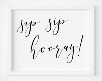 May include: A white framed print with black calligraphy that reads "sip sip hooray!"
