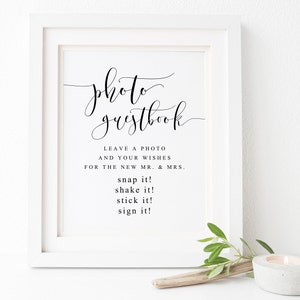 May include: A white framed sign with black text that reads "photo guestbook". The text below says "Leave a photo and your wishes for the new Mr. & Mrs. snap it! shake it! stick it! sign it!"