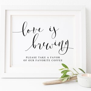 Puede incluir: Un cartel enmarcado en blanco con caligrafía negra que dice "love is brewing" y el texto "Please take a favor of our favorite coffee".