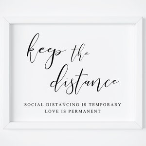 May include: White framed print with black calligraphy that reads "keep the distance" and the text "Social distancing is temporary, love is permanent."