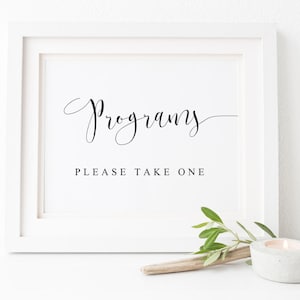 May include: A white frame with a sign that says "Programs" in a cursive font. Below the word "Programs" is the text "Please Take One".