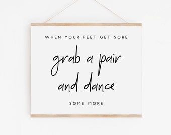 May include: A white sign with a wooden frame hangs on a white wall. The sign reads "When your feet get sore grab a pair and dance some more".