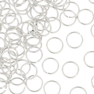 May include: A large pile of silver jump rings, a type of jewelry finding, scattered on a white background.