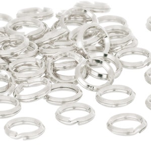 Op de afbeelding: Een stapel zilveren springringen, een soort sieradenbevestiging, verspreid over een witte achtergrond.