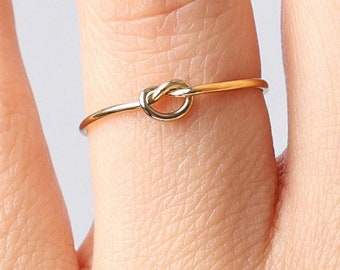 May include: A simple gold knot ring worn on a finger.