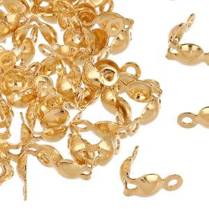 May include: A collection of small, gold-colored jewelry findings, including crimp end caps and connectors. The findings are made of a shiny, metallic material and are scattered across a white surface. The end caps have a curved shape with a loop.