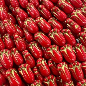 Pode incluir: Um close-up de uma coleção de contas de vidro vermelhas com detalhes dourados. As contas têm o formato de tulipas e um acabamento brilhante.
