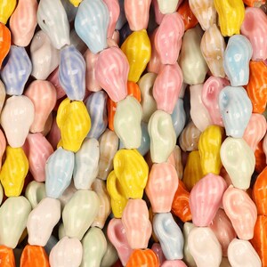 May include: A close-up of a collection of colorful, glazed ceramic ear-shaped candies. The candies are in various pastel colors, including yellow, pink, blue, orange, and white. The candies are arranged closely together, filling the frame.