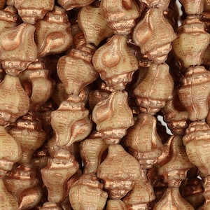 May include: A close-up of a pile of small, white seashell-shaped beads with a copper metallic finish.