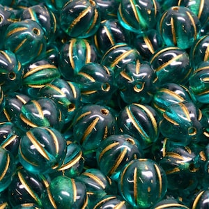 May include: A close-up of teal green glass beads with gold accents. The beads are oval shaped and have a textured surface.