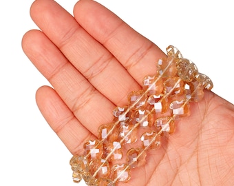 May include: A bracelet made of amber-coloured, faceted beads, arranged in a floral design. The bracelet is held in an open hand. The beads are strung together. The background is white.