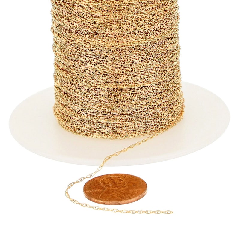 May include: A spool of gold-colored chain, with a length of chain laid out next to a US penny for scale.