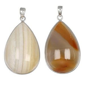 May include: Two teardrop-shaped pendants with silver-colored metal settings. One pendant features a cream-colored stone with vertical stripes. The other pendant has a brown and orange stone with a polished surface. Both have a silver loop at the top.