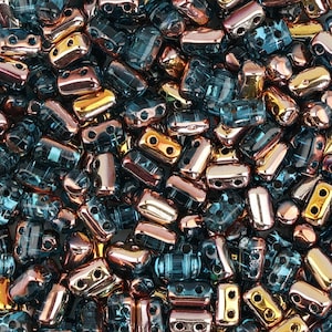 May include: A close-up image of a large quantity of small, rectangular glass beads. The beads are a mix of teal blue and copper colors with a shiny, iridescent finish.