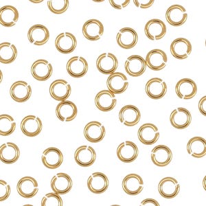 May include: A scattering of gold jump rings, a type of jewelry finding, on a white background.