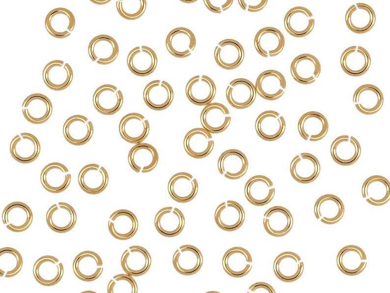 May include: A scattering of gold jump rings, a type of jewelry finding, on a white background.
