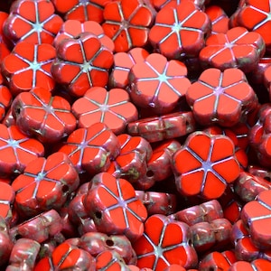 May include: A close-up of a pile of red flower-shaped beads. The beads have a glossy finish and a white outline.