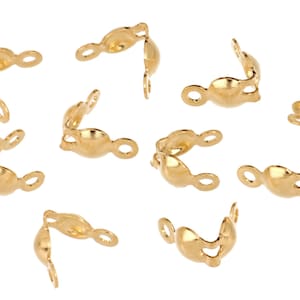 May include: A collection of gold-colored crimp end findings, scattered against a white background. Each finding has a curved shape with a loop on one end and a small opening on the other, designed for jewelry making.