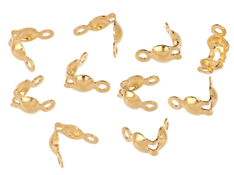 May include: A collection of gold-colored crimp end findings, scattered against a white background. Each finding has a curved shape with a loop on one end and a small opening on the other, designed for jewelry making.