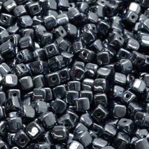 May include: A close-up view of a pile of small, square, black glass beads. The beads have a shiny, reflective surface.